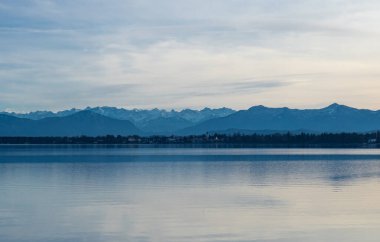 Beautiful scenery at lake Starnberger See, Germany: The flat water surface of the lake in front of forests and high alpine peaks.