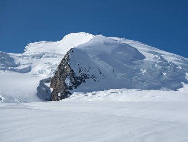 İsviçre 'nin Valais kentindeki Strahlhorn zirvesinde güneşli bir sabah: Mavi gökyüzünün altında sabahleyin kar altında geniş buzullu arazi