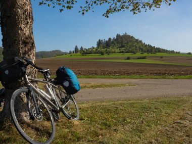 Cycling along Schwaebische Alb cycling route, passing Kornbuehl peak in Burladingen, Germany, is a highlight. A touring bike in front of the round hill with St. Anne chapel clipart