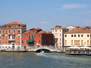 İtalya 'nın Venedik kıyısındaki tarihi renkli konut binaları. Evlerin arasındaki küçük bir su kanalına girmek için yürüyen köprüden geçen bir tekne..