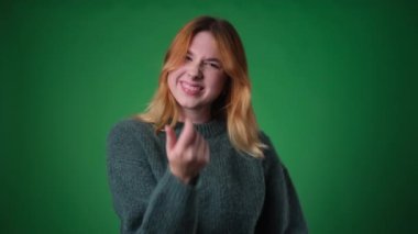 Neşeli genç bir kadın, gelişigüzel giyinmiş, neşeli bir şekilde birisini, canlı yeşil bir arkaplana karşı bir jest yapmaya davet ediyor. Canlı ifadeler ve davetkar tavırlar bir eğlence duygusu iletir..