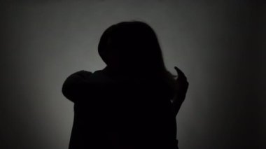 Genç bir çiftin, siluetleri sakin, gri bir arka planda sarmaş dolaş olurken şefkatle kucaklaşması. Gölgeli figürler samimiyet ve samimiyet hissi veriyor..