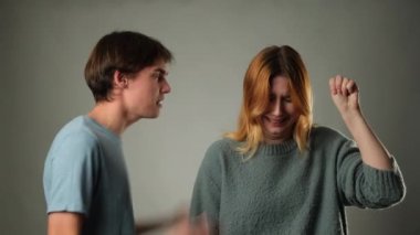 Erkek öfkeyle sesini yükseltirken, bir kadın, gri bir zemine karşı, yalvararak yardım için işaret veriyor. Çelişkili hareketler, duygusal gerilim ve potansiyel çatışma sahnesi yaratır..