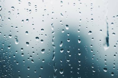 Camdaki yağmur damlaları, arka plandaki bulanık manzara