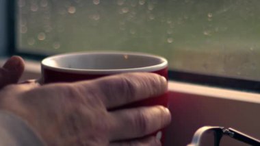 Woman with hot drink looks out of window in the rain close up zoom shot slow motion selective focus