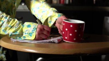 Woman with hot drink writing in notepad on kitchen table medium 4k shot selective focus