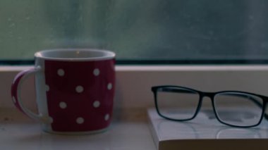 Hot drink and book in the window on rainy day close up 4k shot slow motion selective focus