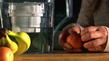 Woman with water filter jug in kitchen with fresh water and fruit medium shot slow motion zoom selective focus