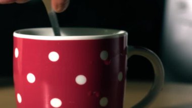 Stirring mug of hot coffee in colorful mug close up shot slow motion zoom selective focus