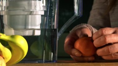 Woman with water filter jug in kitchen with fresh water and fruit medium shot slow motion zoom selective focus