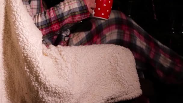 クリスマスミディアムズームショット選択フォーカスでホットドリンクで椅子でリラックスした女性 — ストック動画