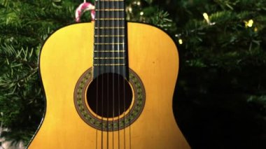 Accoustic guitar in front of Christmas tree medium zoom tilting shot selective focus