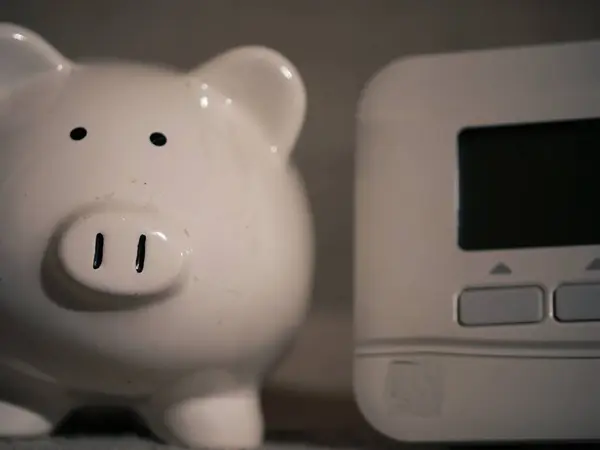 Piggy bank savings and central heating thermostat controls close up shot selective focus