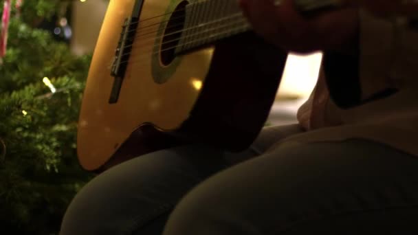 ツリーミディアムズームショット選択的な焦点の前にギターでクリスマスカロルを再生 — ストック動画