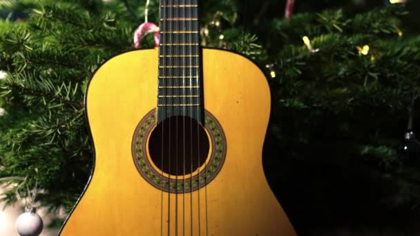 クリスマスツリーの前に音響ギター 中4K傾斜ショット選択的な焦点 — ストック動画