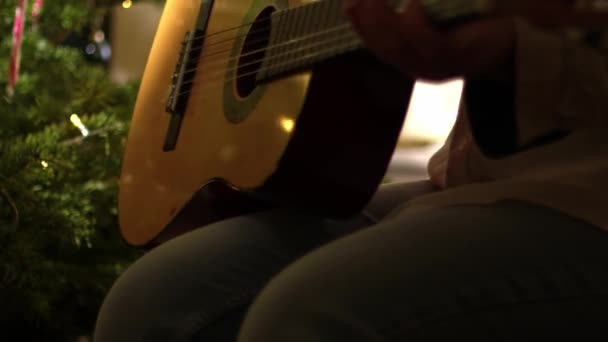 ツリーミディアム4Kショット選択的な焦点の前にギターでクリスマスキャロルを再生 — ストック動画