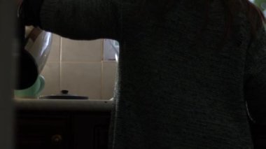 Mutfaktaki su ısıtıcısından sıcak su dolduran kadın yavaş çekim seçici odak noktası.