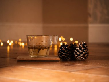 Bir fincan papatya çayı ve parlak ışıklı çam kozalakları arka plan bokeh orta boy seçici odak noktası.