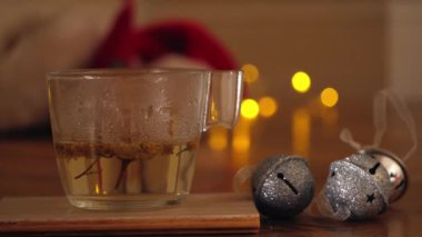 Bir bardak papatya çayı ve pırıltılı ışıklarla süslenmiş Noel mücevherleri. Arka plan, yakın çekim, seçici odaklanma.