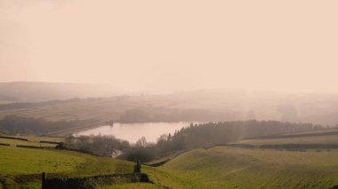 Puslu bir günde Peak District Ulusal Parkı 'ndaki göl ve tarım arazisi 4k hava aracı seçici odak noktası