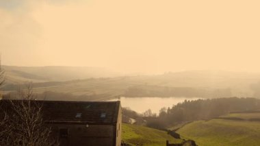 Puslu bir günde Peak District Ulusal Parkı 'ndaki çiftlik evi ve göl geniş 4k hava aracı seçici odak noktası