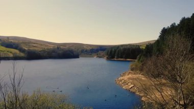 Peak District Ulusal Parkı 'ndaki göl ve tarım arazisi mavi gökyüzü manzarası geniş zoom drone hava seçici odak noktası