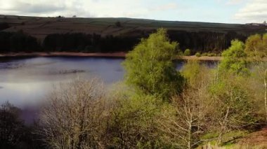 Ağaçlar ve tarım arazileri, Peak District Ulusal Parkı 'ndaki gölü çevreleyen mavi gökyüzü geniş zoom insansız hava aracı seçici odak noktası.