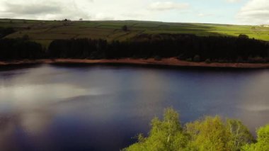 Ağaçlar ve tarım arazileri, Peak District Ulusal Parkı 'ndaki gölü çevreleyen mavi gökyüzü geniş zoom insansız hava aracı seçici odak noktası.