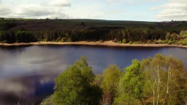 Ağaçlar ve tarım arazileri, Peak District Ulusal Parkı 'ndaki gölü çevreleyen mavi gökyüzü geniş zoom insansız hava aracı seçici odak noktası.