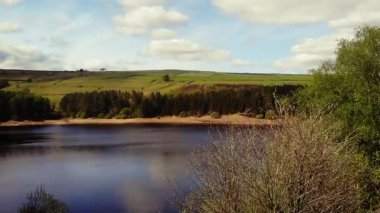 Ağaçlar ve tarım arazileri, Peak District Ulusal Parkı 'ndaki gölü çevreleyen mavi gökyüzü geniş zoom insansız hava aracı seçici odak noktası.