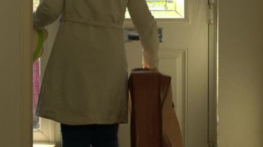 Bavullu kadın eve ön kapıdan geliyor. 4K 'lık seçici bir odaklanma. 