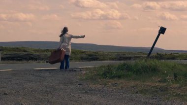 Boş otoyolda bavuluyla otostop çeken bir kadın. 4K 'lık geniş bir açı. 