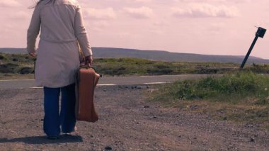 Boş otoyolda bavulla yürüyen bir kadın geniş açılı 4K çekim odaklı. 
