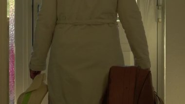 Elinde bavul olan kadın evden ön kapıdan çıkıyor. Orta derece seçici bir odak noktası. 