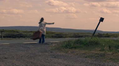Boş otoyolda bavuluyla otostop çeken bir kadın. 4K 'lık geniş bir açı. 