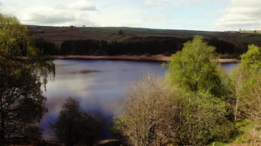 Ağaçlar ve tarım arazileri Peak District Ulusal Parkı 'ndaki gölü çevreleyen mavi gökyüzü geniş 4k paneli insansız hava aracı seçici odak noktası