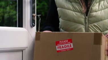 Kırılgan kutu taşıyan bir kadın, orta boy odak noktasında kapıyı çalıyor.