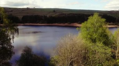 Ağaçlar ve tarım arazileri, Peak District Ulusal Parkı 'ndaki gölü çevreleyen mavi gökyüzü geniş zoom insansız hava aracı seçici odak noktası.