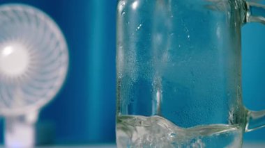 Pouring ice water with desk fan on cool blue background close up 4k shot selective focus