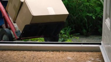 Delivery of cardboard boxes and trolley cart outside of home front door medium zoom shot selective focus