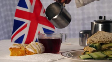 Geleneksel İngiliz çayına kek ve salatalıklı sandviçle süt dökmek seçici bir odak noktası.