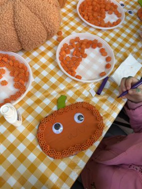 A child at a workshop makes a Halloween pumpkin out of cardboard and pasta