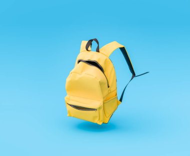 Havada asılı duran canlı sarı bir sırt çantasının 3D görüntülenmesi sağlam bir mavi arkaplan, eğitim ve öğrenim kavramı.