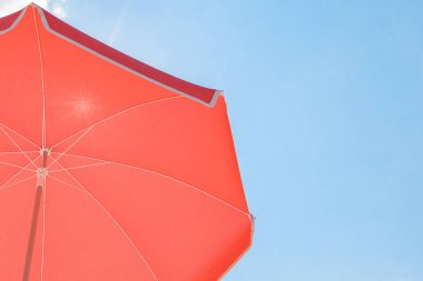 Parlak kırmızı güneş şemsiyesinin 3 boyutlu yansıması açık mavi gökyüzüne karşı gölge sunuyor, yaz günlerinde güneş koruması konsepti.