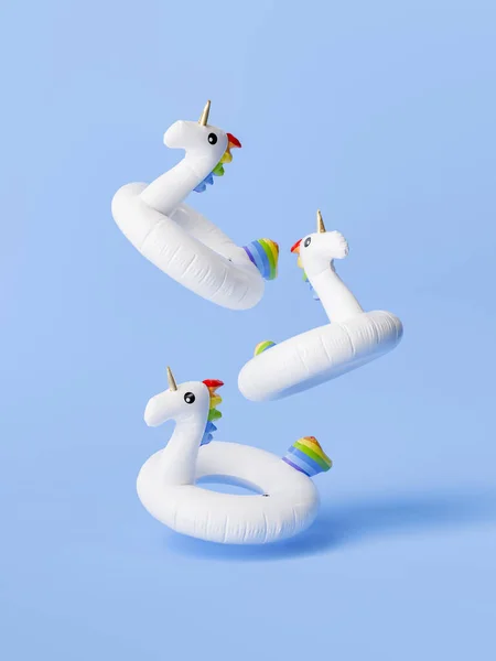 3d rendering of three white unicorn pool rings with colorful details floating midair against a clear blue background. Whimsical summer concept.