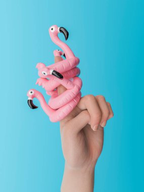 Mavi arka planda, parmağında pembe flamingo yüzükler tutan bir el. Yaz ve eğlenceli aksesuar konsepti. 3d oluşturma.