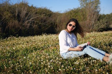 Çiçek tarlasında oturan bir kadın, kitap okumaktan hoşlanıyor..