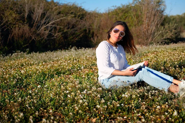 stock image Woman sitting in a field of flowers, enjoys reading a book.