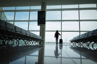 Elinde bavul olan bir kadın, uçağını beklerken havaalanı penceresinden dışarı bakıyor..
