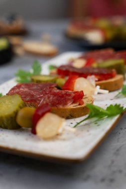 Tuzlu mezeler, turşu ve dilimlenmiş sosis, beyaz tepside servis edilir..